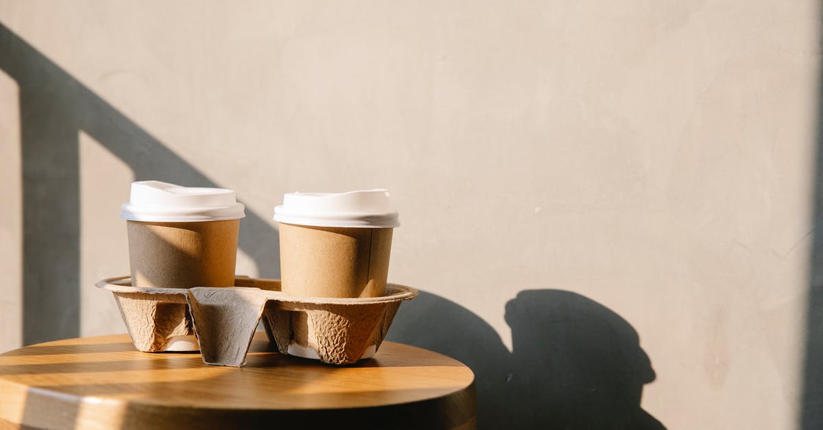 Difference in caffeine levels between light and bold coffee? - Cofee paper cups with plastic lids on holder tray on brown wooden table casting a shadow at sunny day