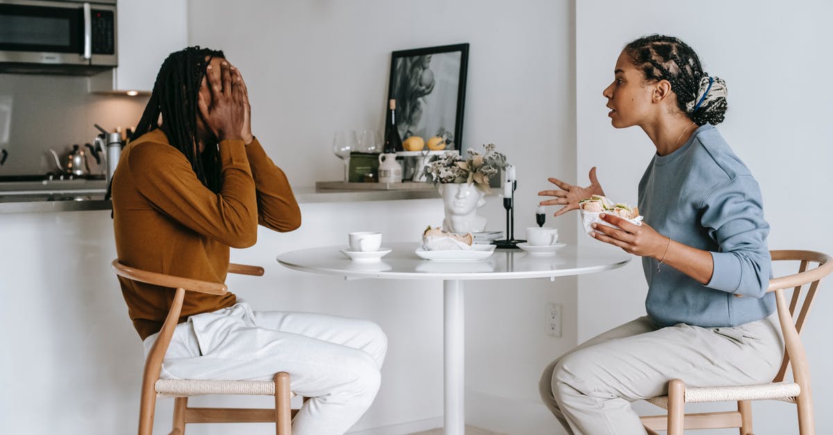 Do all blenders have the problem of food sticking to the side away from the spinning blades? - Side view of expressive Hispanic female in casual clothes arguing with African American boyfriend covering face with hands while sitting at table in kitchen at home