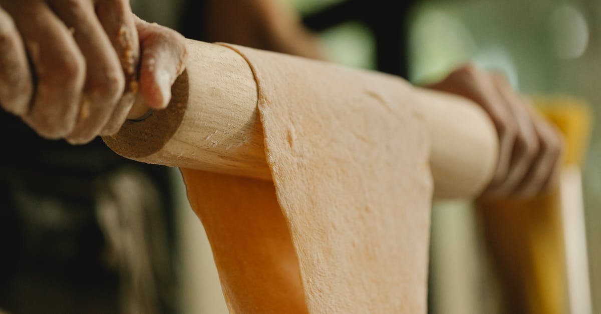 Do bakeries generally knead dough for bread by hand or use a machine? - Low angle of unrecognizable person stretching soft dough on rolling pin while preparing food in kitchen