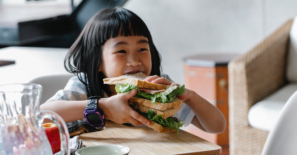 Do bread bins really keep homemade breads fresh? [duplicate] - Asian child sitting at wooden table during breakfast and eating tasty sandwich with lettuce leaves