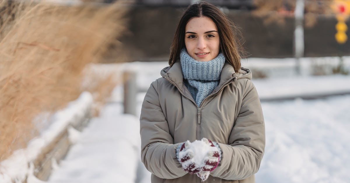 Do I have to wait for frozen steak to defrost? - Content young female wearing warm clothes and mittens in warm clothes holding snow in hands spending winter day in city park and looking at camera