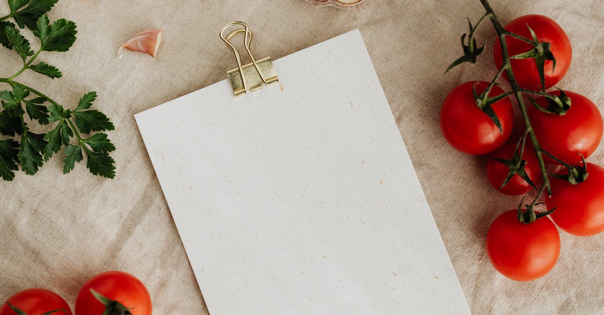 Do you need to cook tomato puree? - From above of blank clipboard with golden paper binder placed on linen tablecloth among tasty red tomatoes on branches together with cutted garlic and green parsley devoted for recipe or menu placement