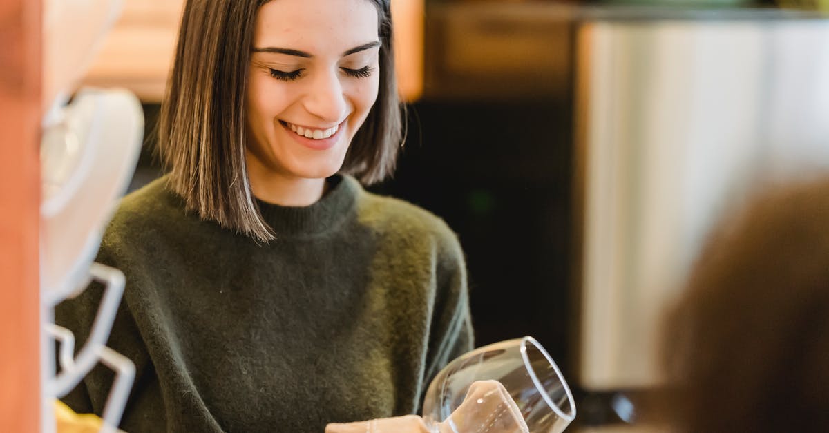 Do you use paper or cloth towel for patting a meat dry before frying? - Crop cheerful female smiling and drying clean transparent glass with fabric on blurred background of kitchen