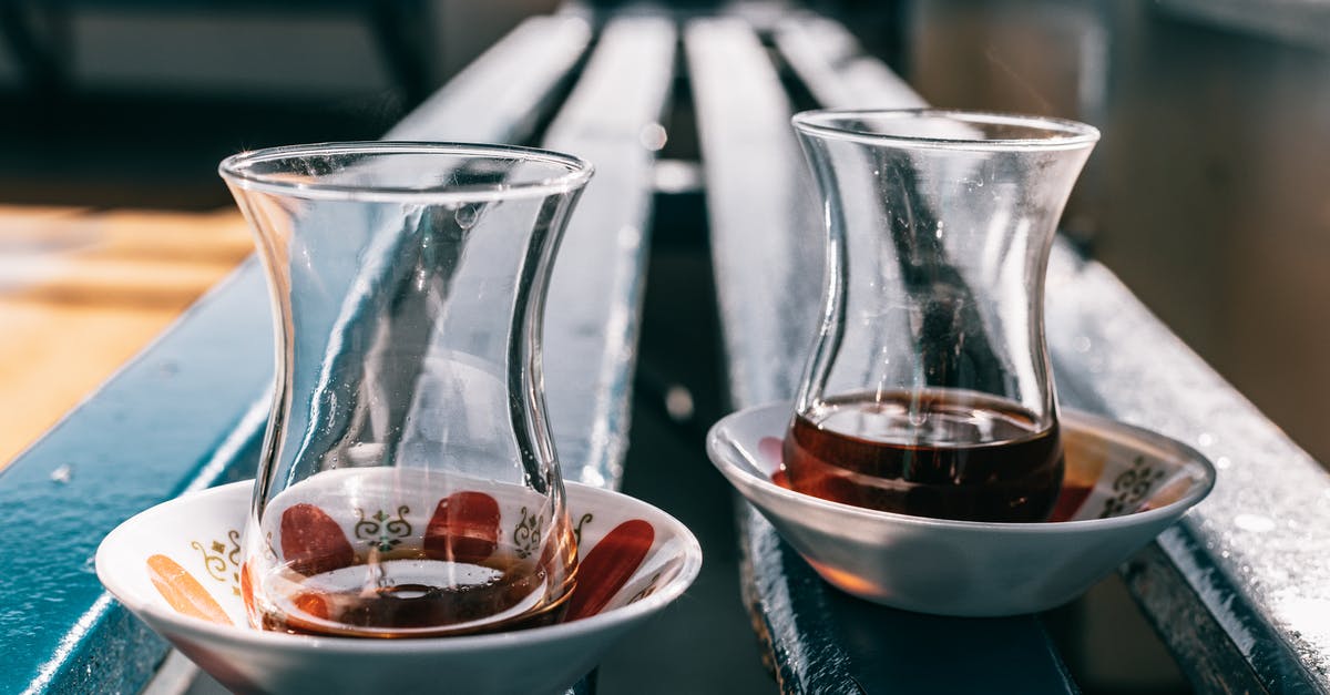 Does a double walled glass mug really keep the liquid warm? - Perspective view of transparent glasses with hot drink served on plates placed on wooden blue bench in room against blurred background