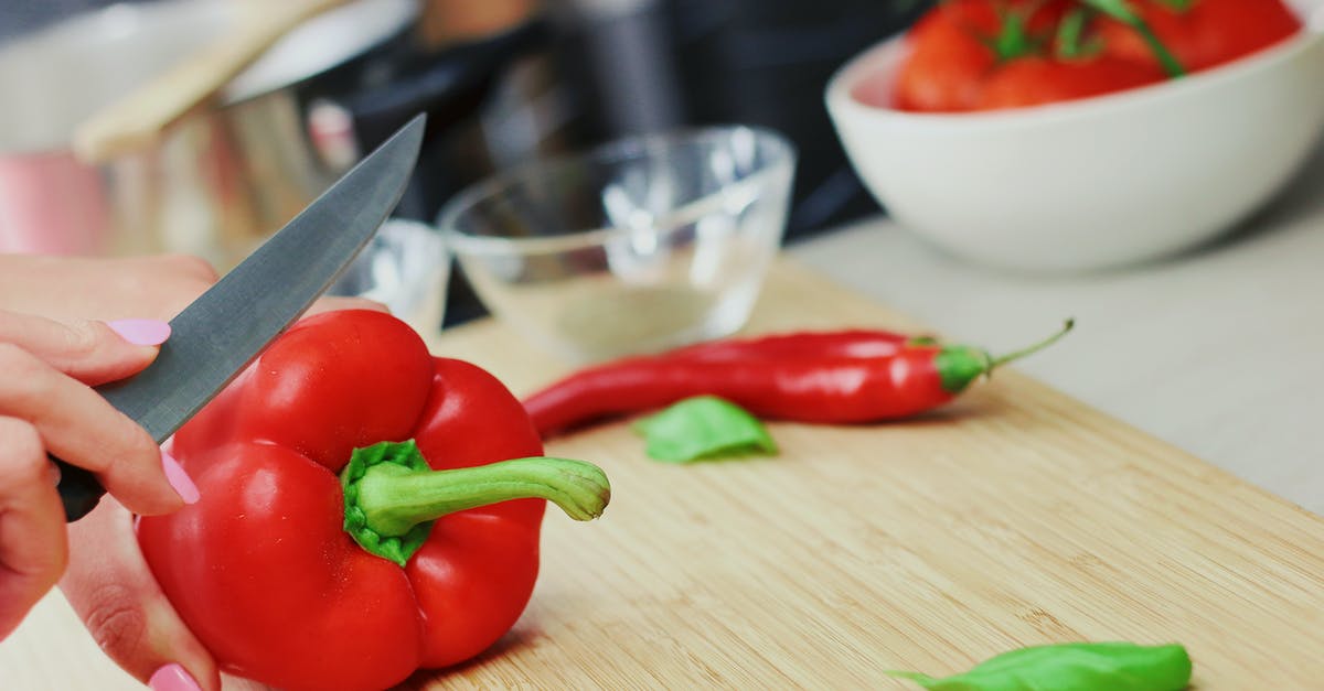 Does chilli get milder with cooking? - Person Slicing Red Chili Pepper on Brown Wooden Chopping Board