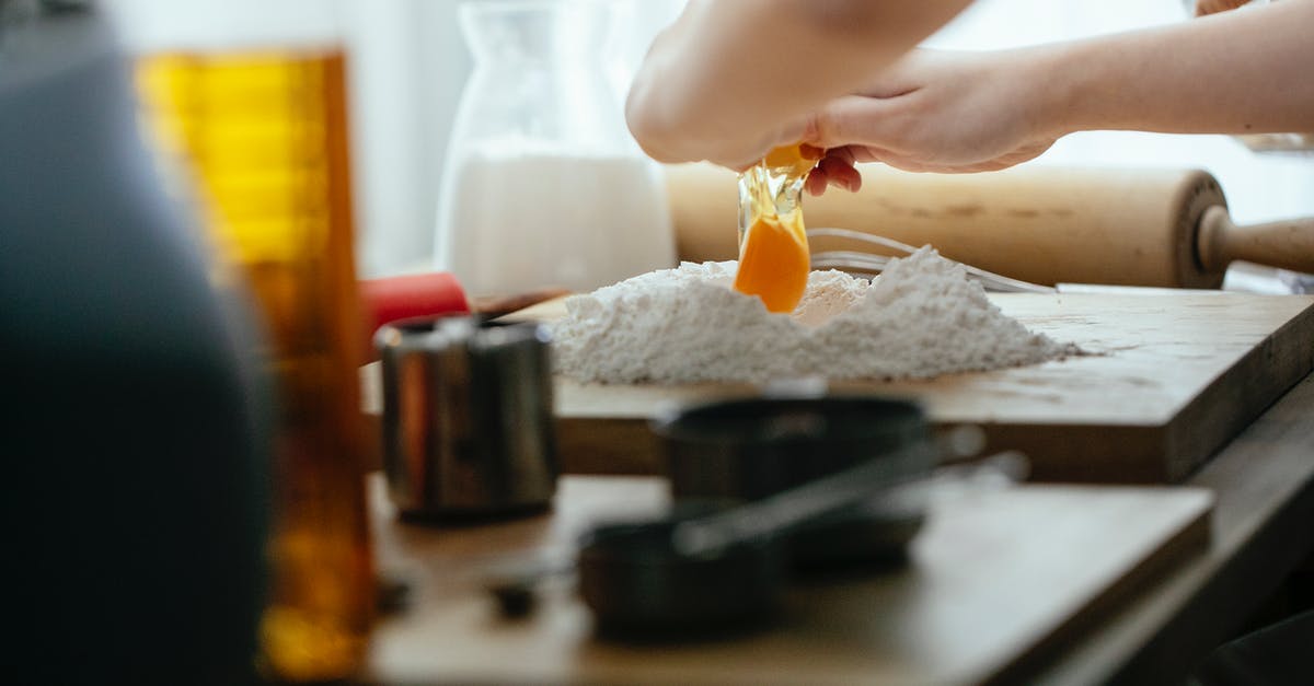 Does handling a lot of flour cause fingernails to break? - Unrecognizable cook breaking egg into pile of flour on wooden board while preparing dough at table in kitchen against blurred background