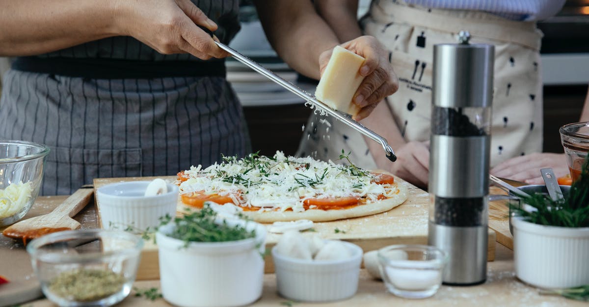 Does it make any sense to grate the radish on a grater without peeling its skin? - Unrecognizable female cooks grating cheese on homemade pizza at table with various ingredients and condiments in kitchen during cooking process