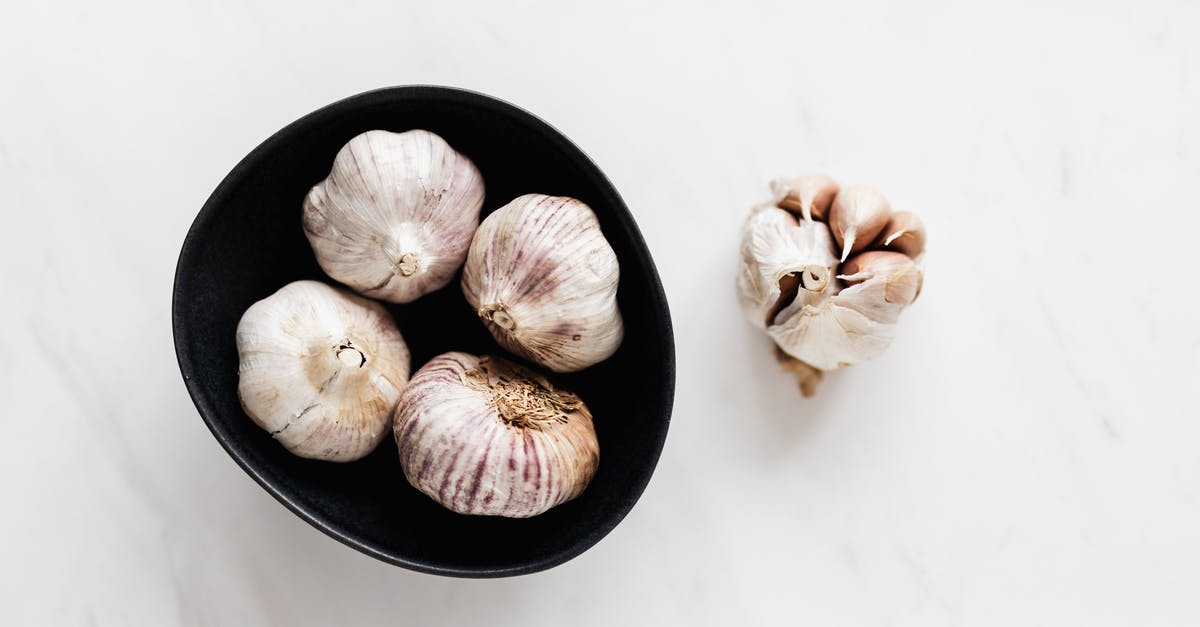 Does roasted garlic leave no aftertaste and smell - Top view of aromatic raw unpeeled garlic in black bowl near half peeled garlic bulb placed on white marble table