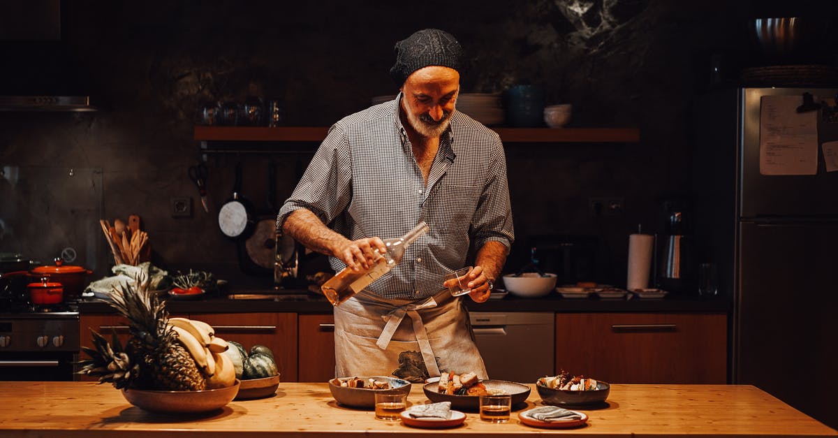 Does the alcohol in wine affect cooking process? - Aged male in apron pouring wine into shot glass while standing at table and assembling order in kitchen