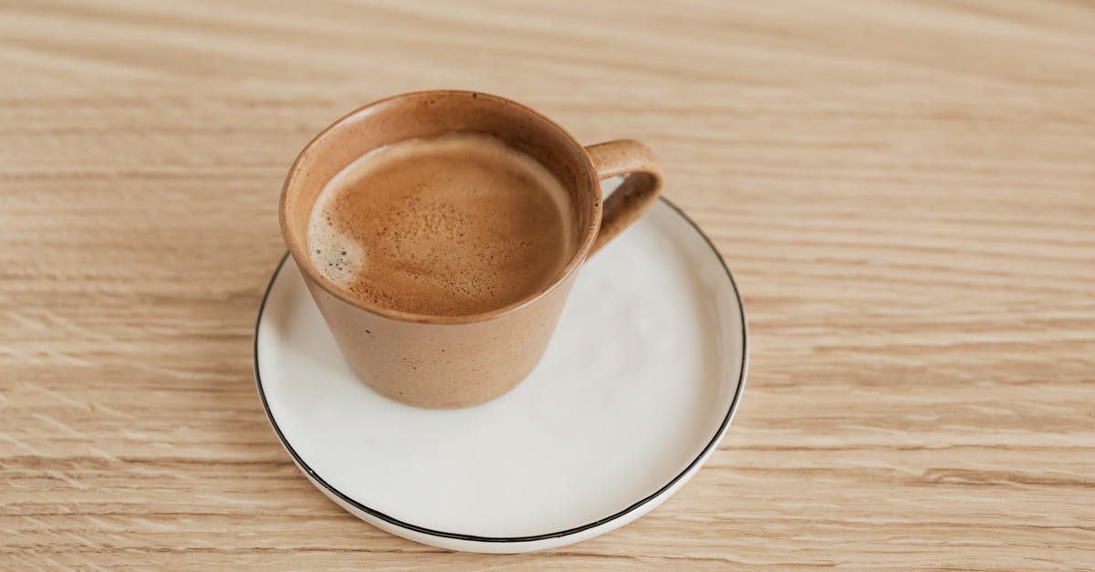 Does the foam from instant coffee always taste bitter? - From above of beige ceramic cup of aromatic espresso on white elegant saucer with thin black edge placed on wooden surface