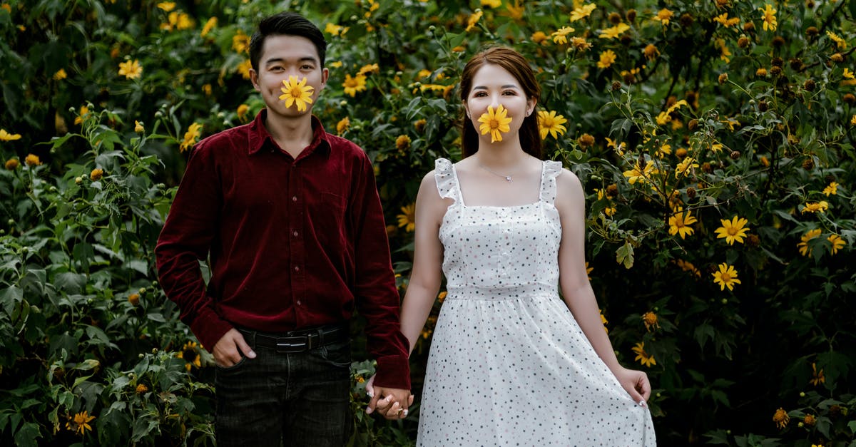 Does the PH in your mouth affect taste? - Happy young Asian couple looking at camera in meadow of bright flowers with green foliage