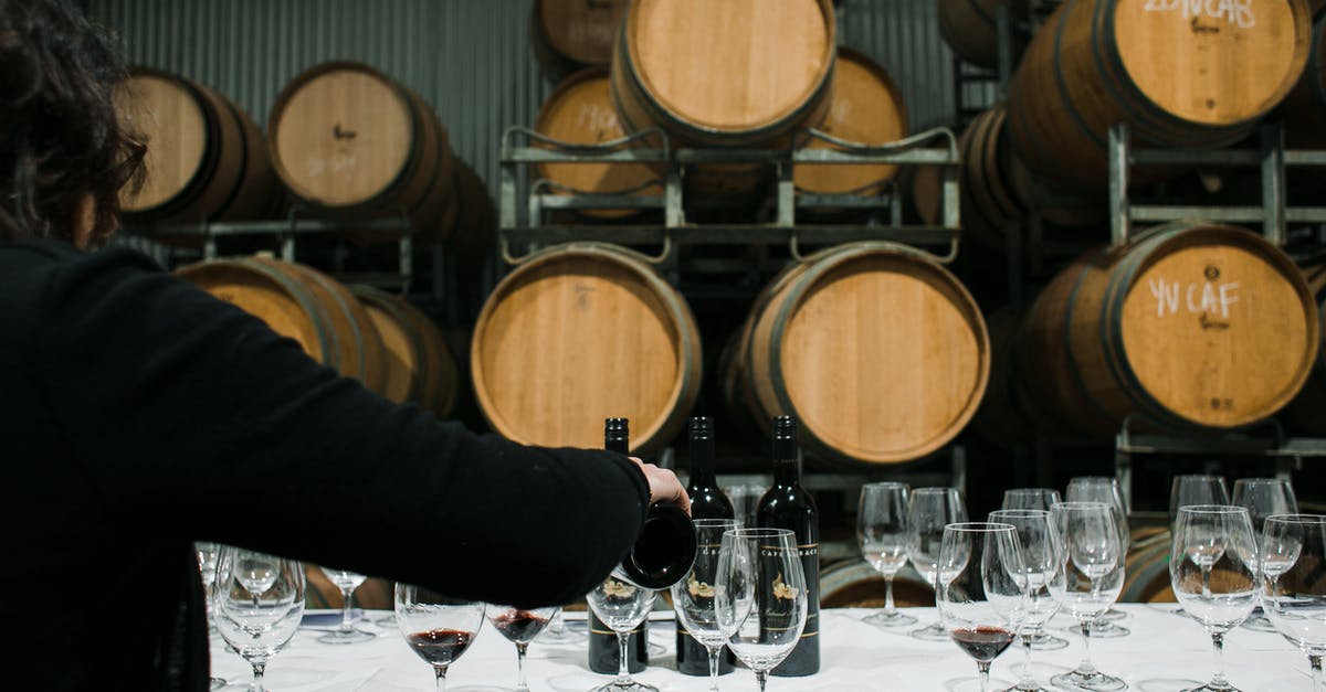 Does the vendors’ storage method affect shellfish quality? - Back view of anonymous sommelier pouring wine from bottle into wineglass while standing at table with glassware in winery against barrels