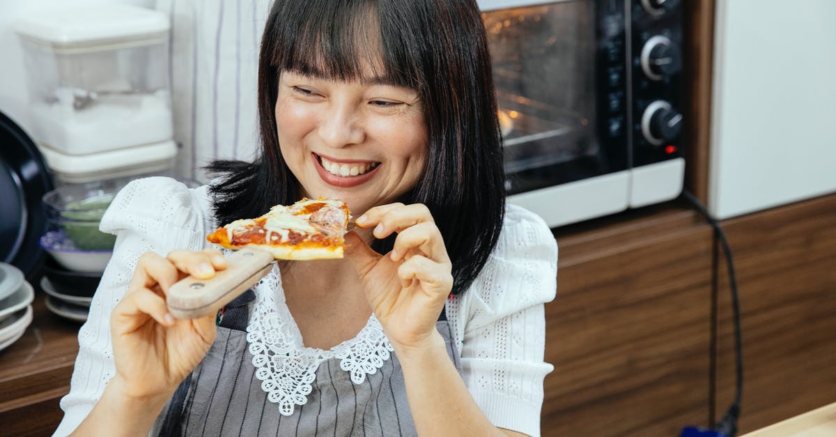 Does there exist a chemical-free, homemade substitute to deli? - Happy Asian woman enjoying eating slice of cheesy pizza sitting at table in kitchen