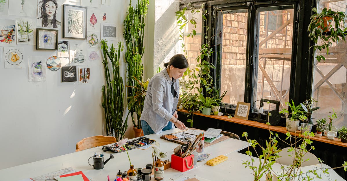 Does this picture accurately describe different kind of coffee? - Side view of female designer creating drawings at desk with collection of felt pens and papers near wall with artworks and plants on windowsill in daylight