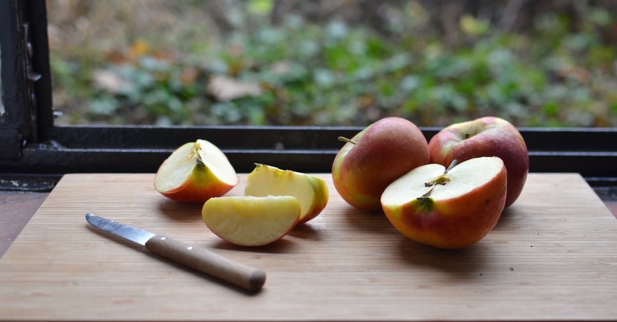 Does this tool where a knife edge is dragged between two angled abrasive pieces hone or sharpen? - High angle of cut red apples placed on wooden cutting board with knife near window