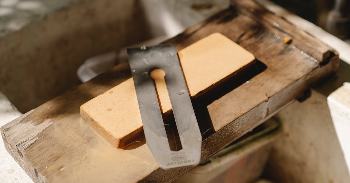 Does this tool where a knife edge is dragged between two angled abrasive pieces hone or sharpen? - From above of sharp knife from jointer for cutting wood placed on wooden plank in professional studio on blurred background