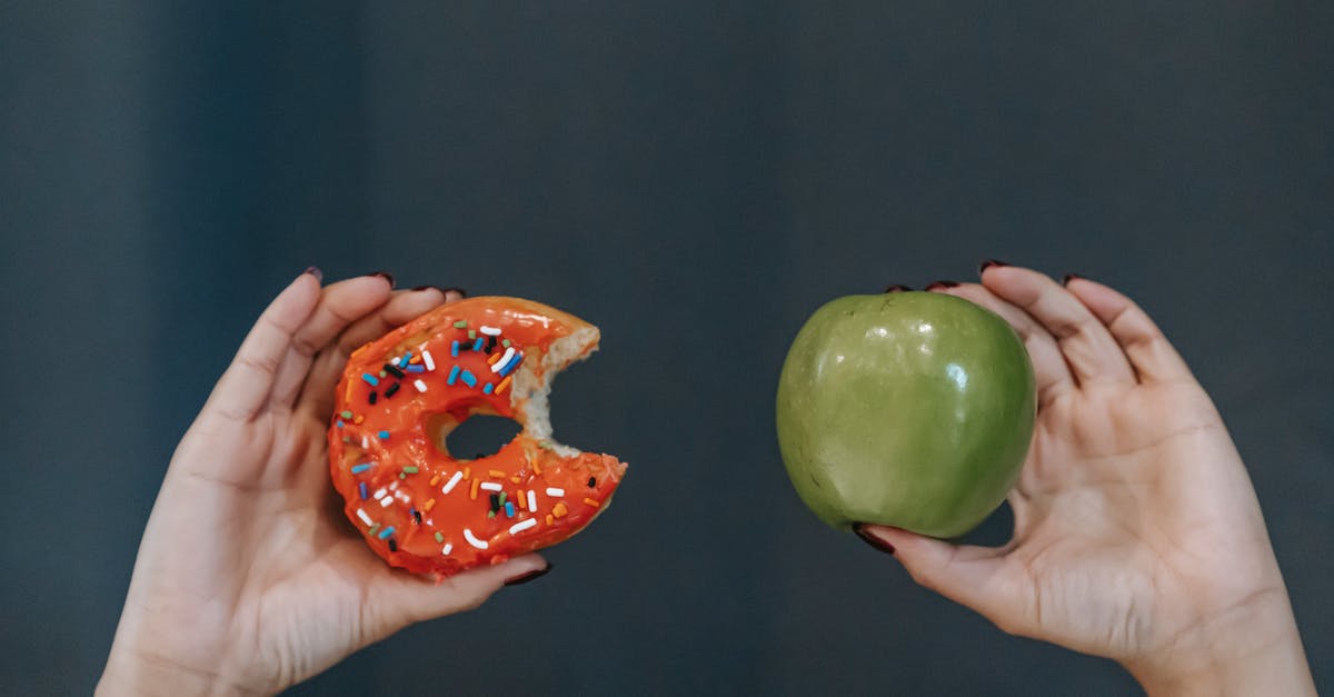 Donut-style Glaze Cracking - Crop unrecognizable young female demonstrating bitten high calorie doughnut and healthy green apple against gray background