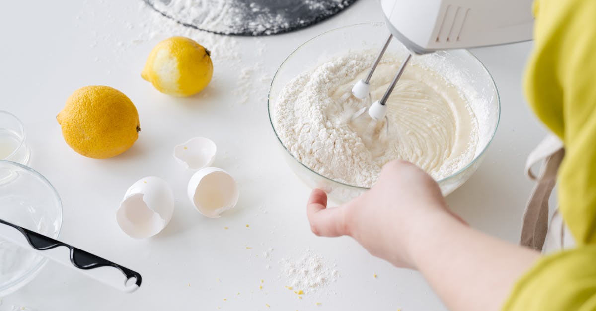 Dough getting into handheld mixer - From above of crop anonymous female with mixer preparing cake dough at table with fresh lemons and eggshells in house