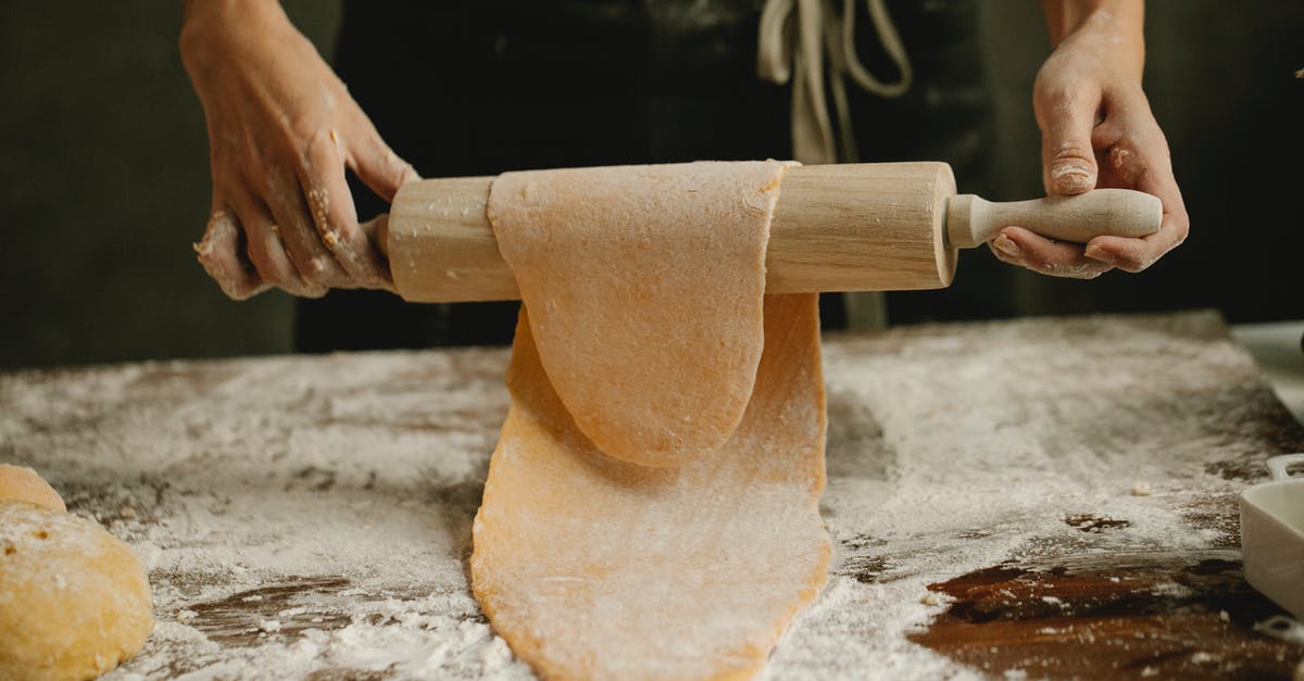 Dough is super springy and sticky. Tears while stretching - Unrecognizable female stretching soft egg dough on rolling pin while making homemade pasta in kitchen