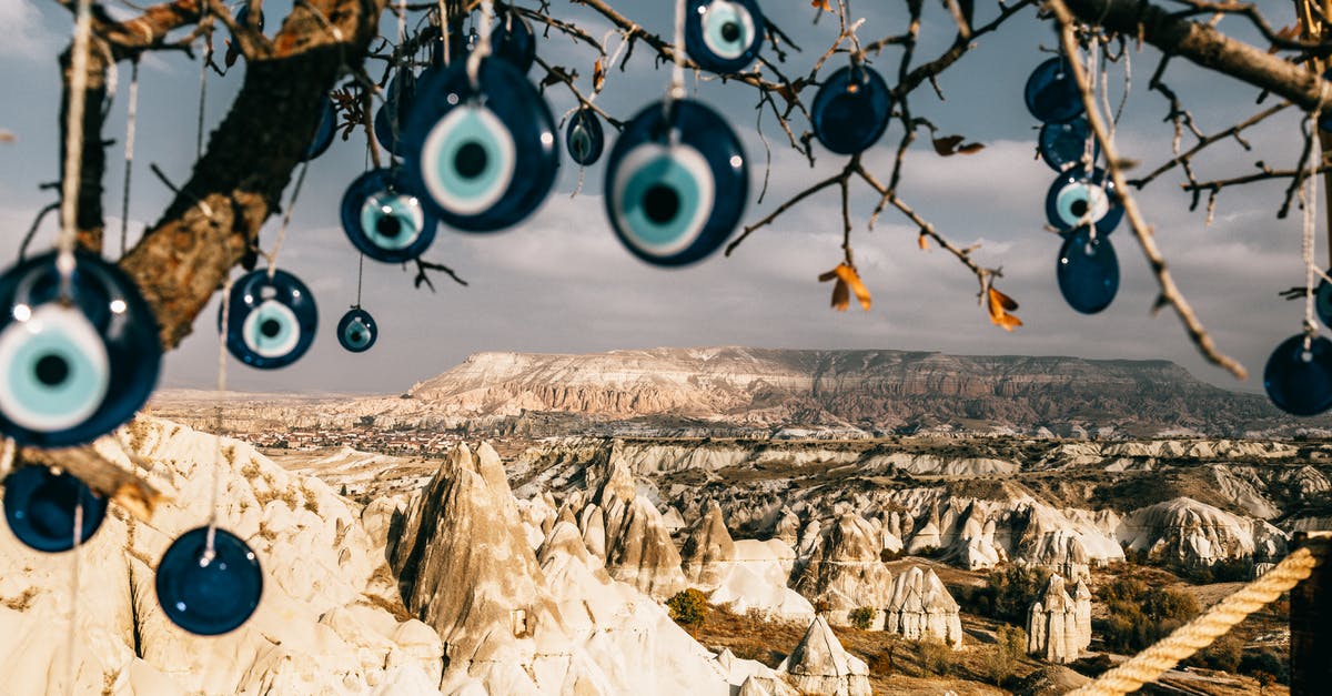 Dry Brining Turkey - Nazar amulets on threads hanging from tree branches near rocky uneven formations with mountains and grass with plants in Turkey in Cappadocia region under gray cloudy sky in summer day