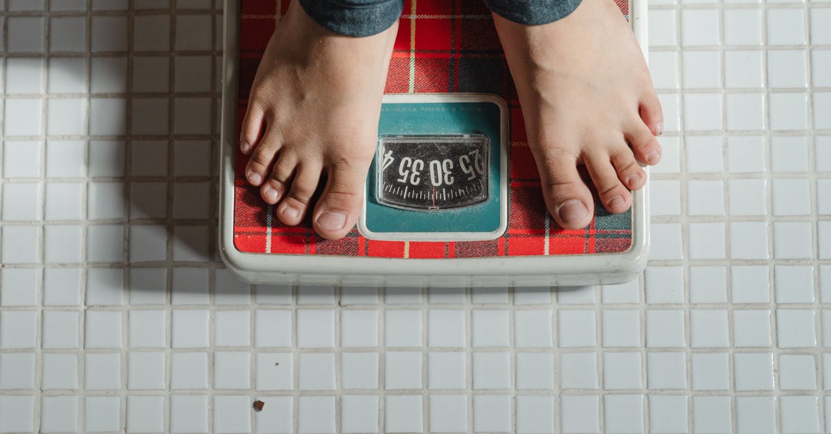 Dry measurement and conversion to weight - From above crop anonymous barefoot child in jeans standing on weigh scales on tiled floor of bathroom