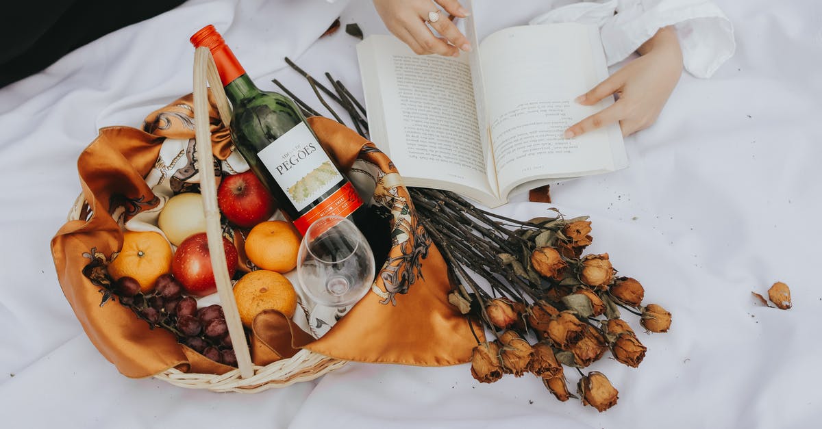 Drying fruits with a household dehydrator - A Person Holding a Book Near the Basket with Fruits and Wine Bottle