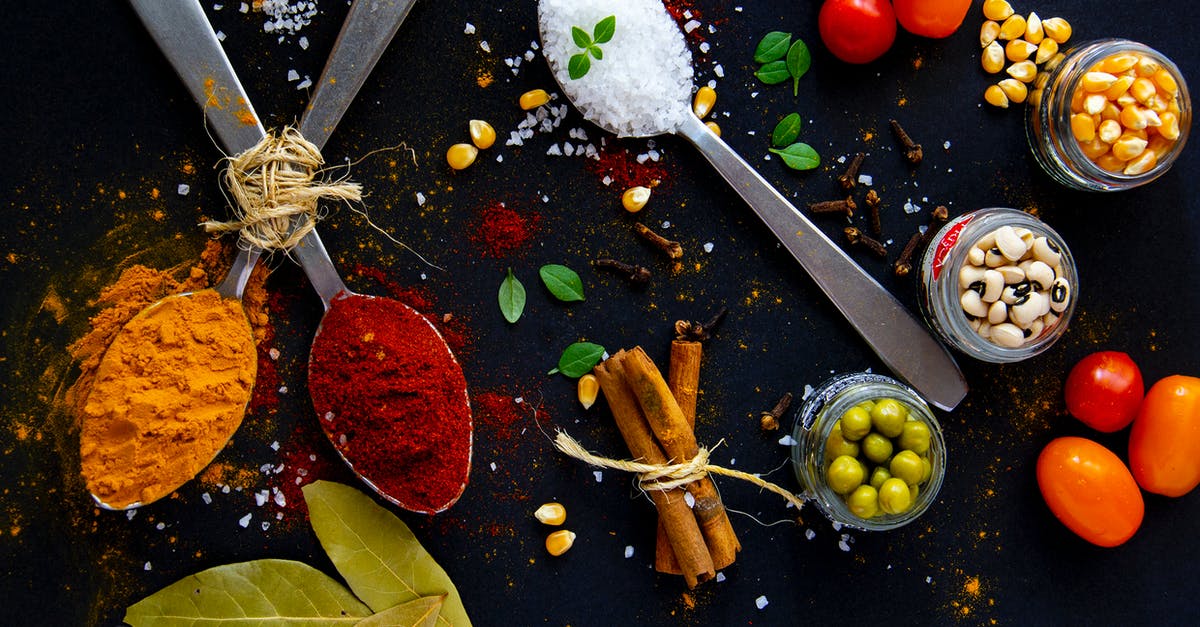 Drying of basil leaf and other herbs - Top view of dry turmeric and paprika near bay leaves with cinnamon sticks and sea salt in spoons near jars with popcorn grains and olives with ripe colorful cherry tomatoes