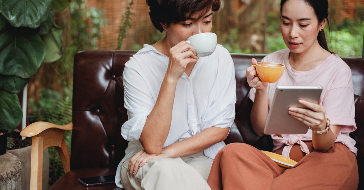 Duration of use for green smoothies - Thoughtful Asian women in casual clothes drinking cups of beverage and looking at screen of tablet