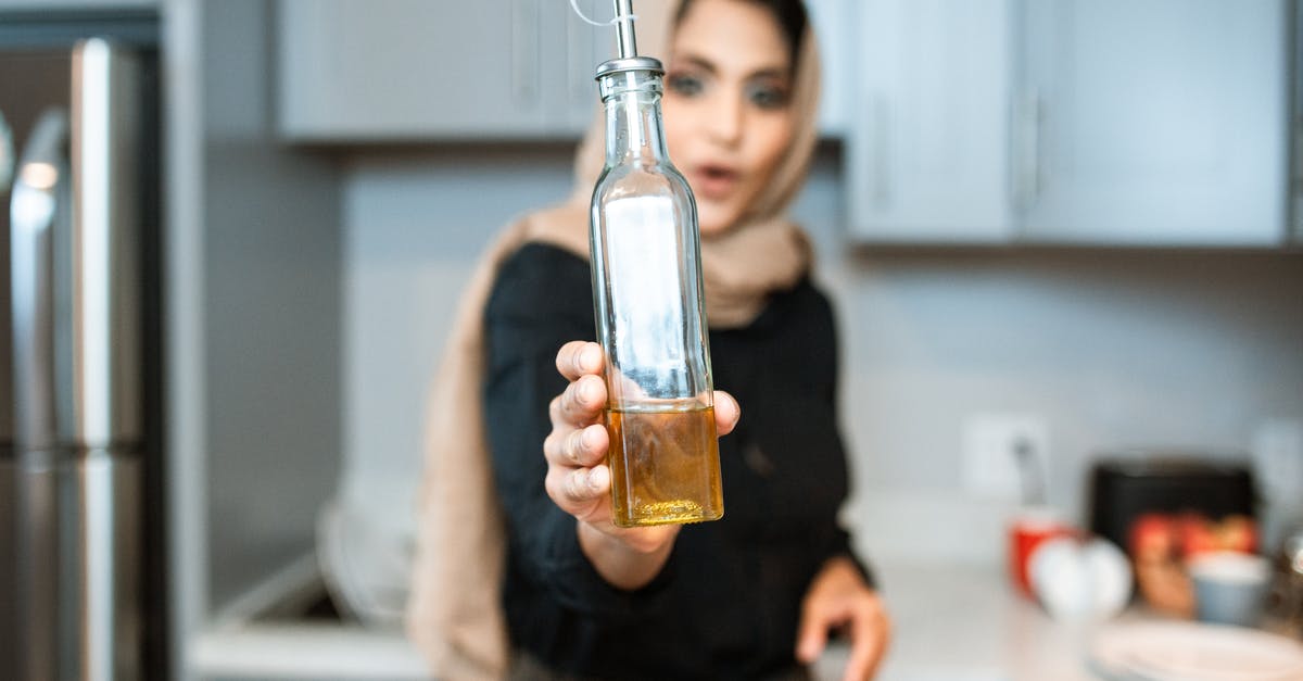 Easiest way to strain fry oil? - Ethnic woman demonstrating bottle of olive oil while cooking