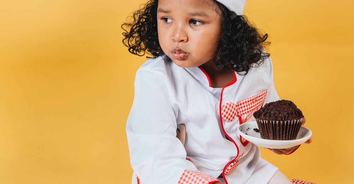 Eating cookie dough - Adorable African American girl in chef uniform and hat eating muffin against yellow background