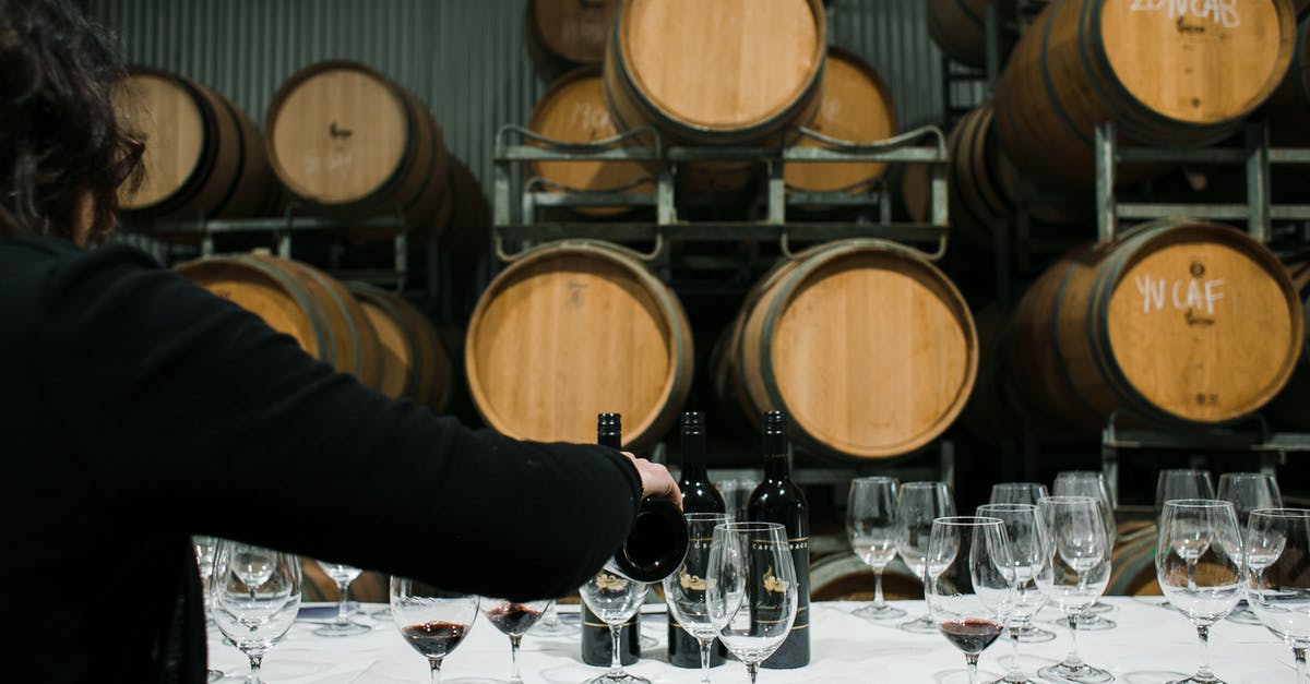 Effects of elevated storage temperature on bread quality - Back view of anonymous sommelier pouring wine from bottle into wineglass while standing at table with glassware in winery against barrels