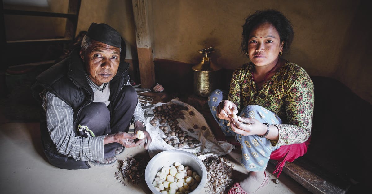 Efficient method to peel raw potatoes - High angle of young and elderly ethnic female in ornamental apparel peeling small potatoes while looking at camera at home