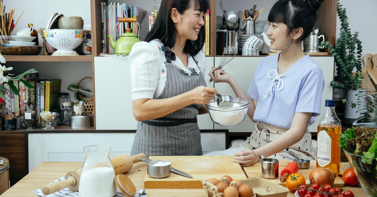 Egg and gluten free custard ideas? - Happy Asian mother wearing apron and daughter standing near wooden counter with ingredients while discussing recipe of pizza