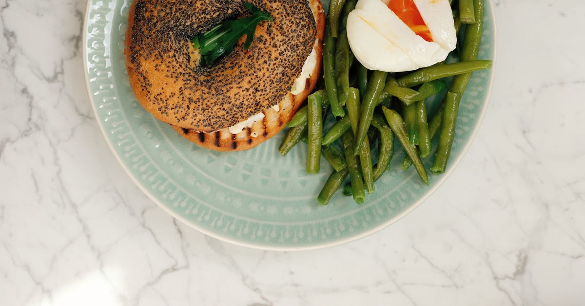 Eggs whites on top and side of yolk - Ceramic plate with tasty fresh bagel and asparagus with poached egg served on white marble table in light modern kitchen at home