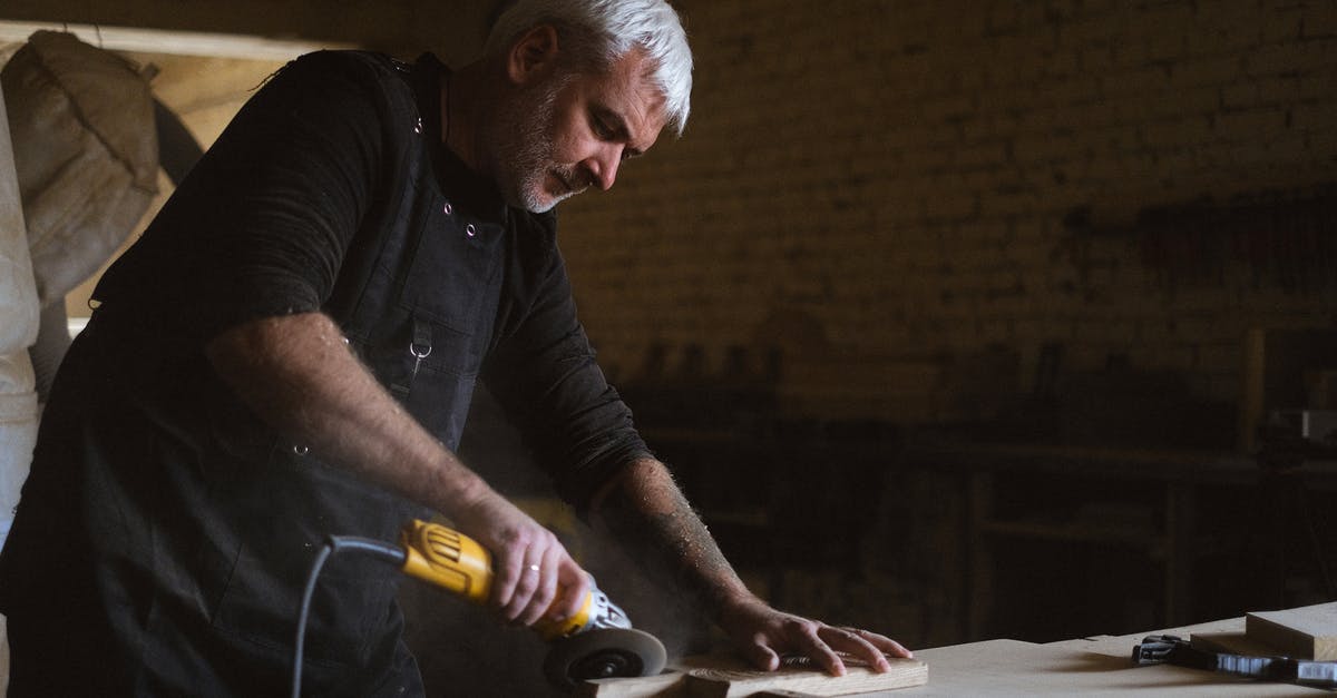 Electric cooktop for sous vide-level precision? - Side view of skilled male master in apron using electric angle grinder to polish wooden plank at table in professional carpentry