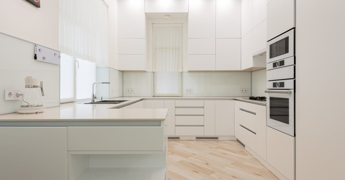 Electric Steam Cooker - Interior of light kitchen with white cabinets and kettle near sink placed against trendy oven and modern appliances in apartment