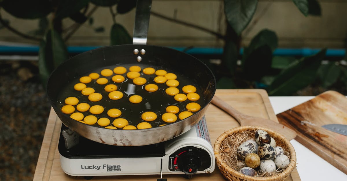 Electric stove coils scratched by pan - From above abundance of small quail eggs frying in pan on cooker on wooden board with heap of eggs in kitchen