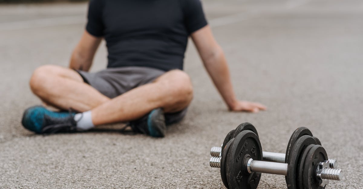 Energy bar is too soft - Crop sportsman resting on road near dumbbells after working out