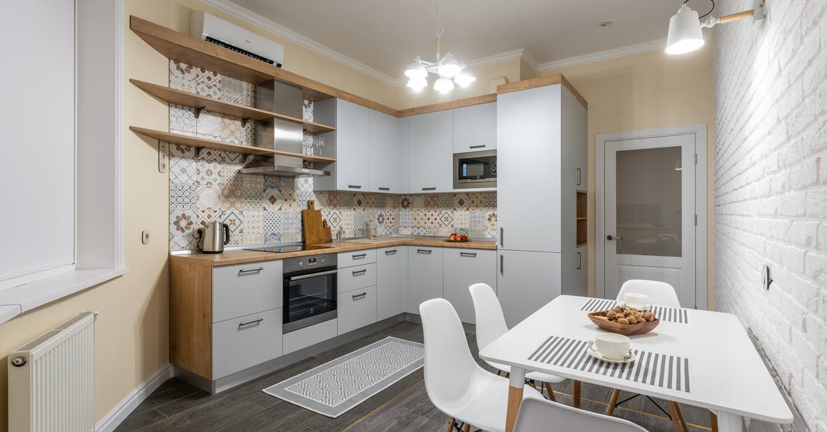 Energy efficiency of microwave and electric kettle for heating water - Modern kitchen with electric appliances and radiator against table with tasty biscuits and cups illuminated by bright chandelier