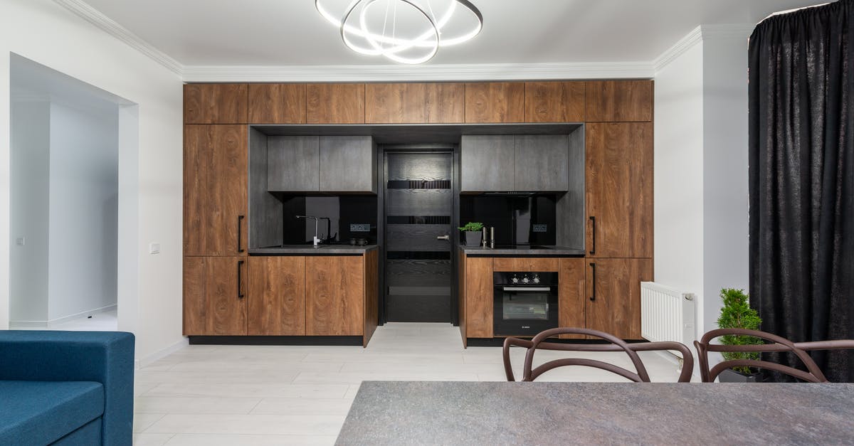 Energy usage of an oven - Creative design of kitchen with cupboards and built in oven against table and sofa in house with geometric lamp