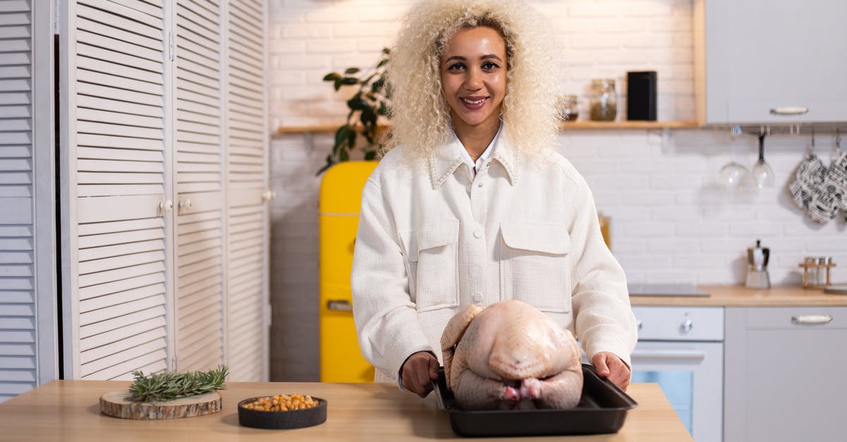 Ensuring dry-brined turkey process is safe - Smiling female looking at camera while standing at counter with uncooked turkey on tray during dinner preparation in modern kitchen