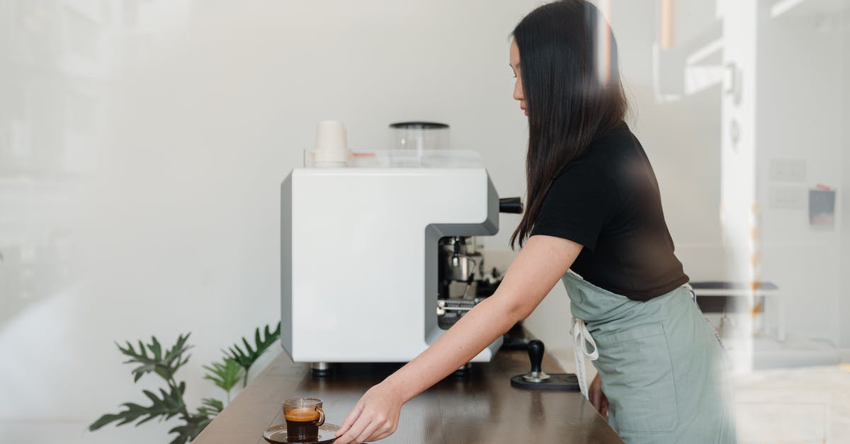 Espresso machine has to warm up halfway through pulling a shot - Side view of concentrated female barista in apron standing nearby professional coffee machine and serving freshly brewed aromatic espresso