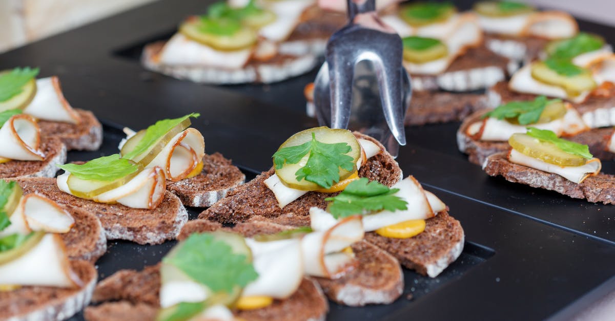 Exploding leaf lard - High angle of crop anonymous person with tongs taking delicious sandwich made of rye bread lard with pickled cucumber and sprig of parsley