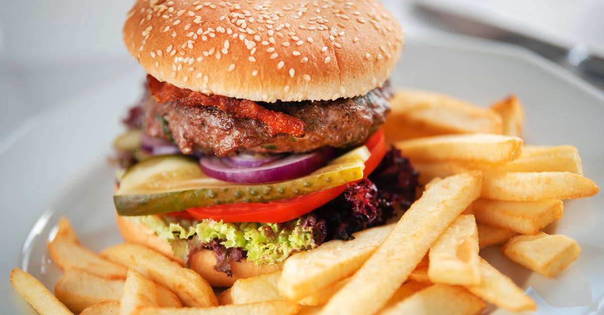 Extremely tender beef at hospital - Tasty burger with juicy patty and tomato with pickle slices between buns with sesame seeds near deep fried potato sticks