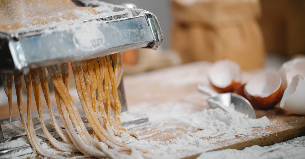 Extrusion pasta maker versus roller: which one makes the best pasta? - Spaghetti produced from iron pasta cutter on wooden table with eggshell and flour on blurred background