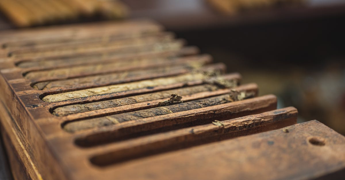 Fabric to be used for cheesecloth - From above closeup of wooden box with narrow rectangular sections with ribbed surface for cigars near table with pile of raw tobacco products in factory