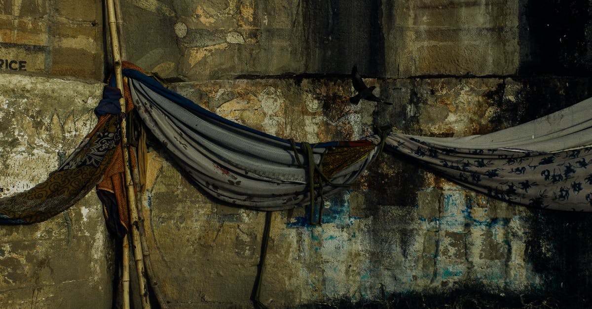 Fabric to be used for cheesecloth - Fabric hammocks hanging on bamboo stick against aged damaged weathered wall of embankment