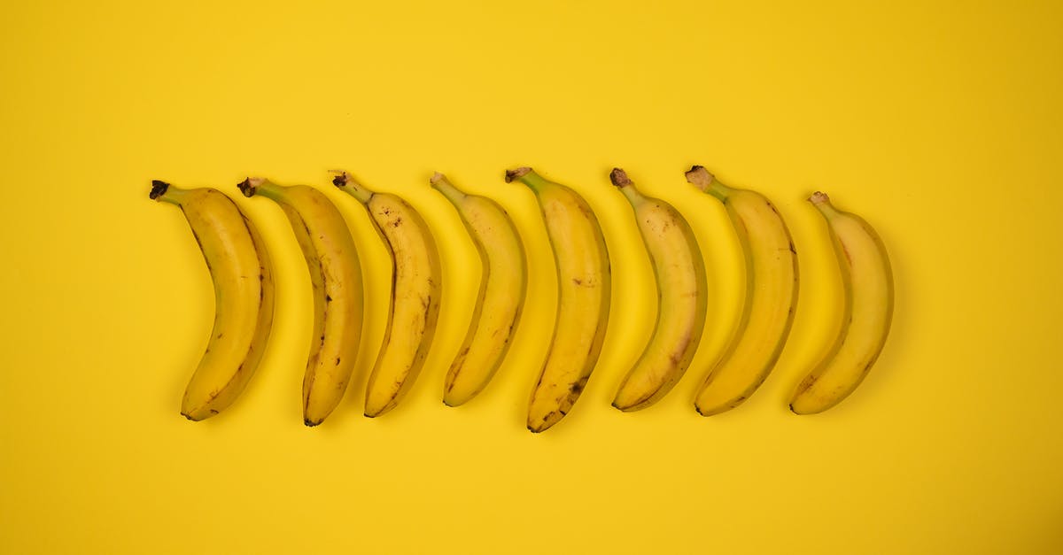 Fastest way to peel 2 dozen bananas? - Top view of tasty ripe bananas with blots on peel composed in row on yellow background