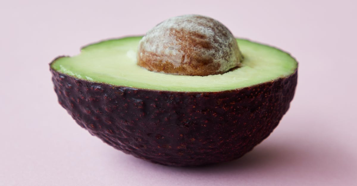 Fastest way to peel and dice vegetables? - Half of avocado with seed on pink surface