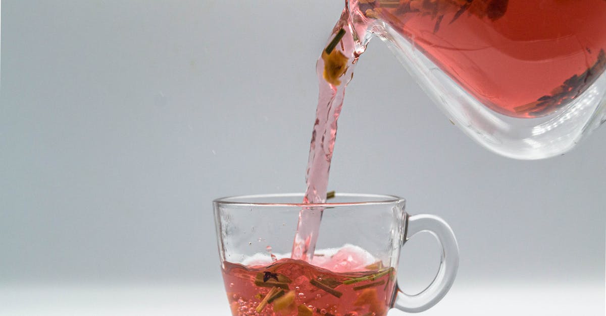 Filling a hot Kettle - Herbal tea with dried leaves and fruit pouring from glass teapot into cup